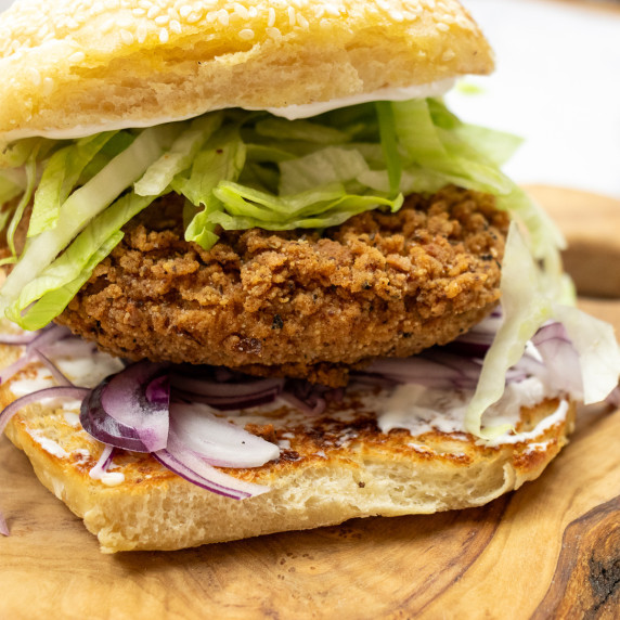 Close up of a crispy looking jackfruit burger in a bun with lettuce, red onion and vegan mayo