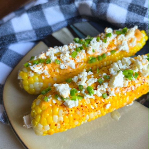 Golden corn topped with white cheese & green jalapenos against a checkered towel