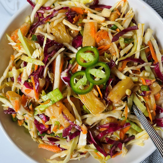 Coleslaw topped with jalapeno slices in a white bowl with a silver spoon.