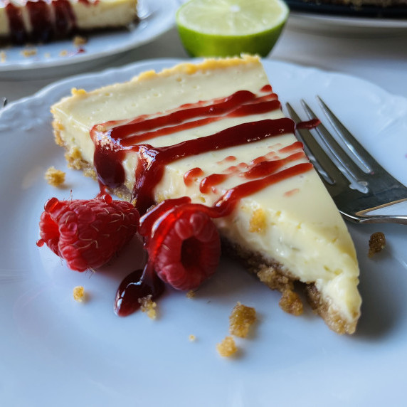 Slice of key lime pie garnished with raspberry sauce and fresh raspberries on a white plate.