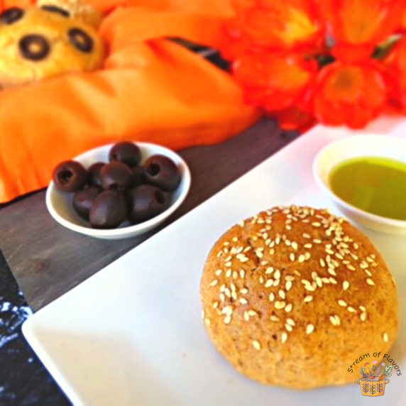 Khobz bread topped with sesame seeds on a white plate with olive oil and olives and a bread basket