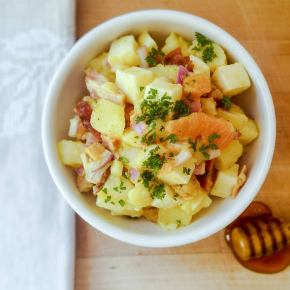 A vibrant Laconian potato salad served in a white bowl, with a honey dipper resting below.