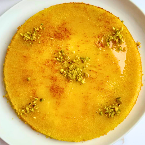 Golden Lebanese Knafeh Na'ameh, soaked in syrup and garnished with pistachios on a white plate.
