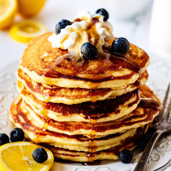 Stack of lemon blueberry pancakes topped with fresh blueberries and whipped cream on a white plate