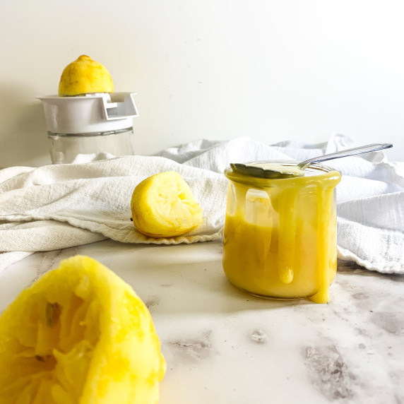 Lemon curd dripping out of a jar with squeezed lemons around on white counter