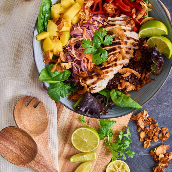 Salad bowl with greens, marinated and fried chicken, mango-lime slaw, coconut chips and lentils