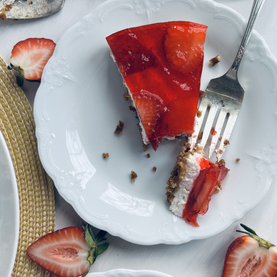 Layered dessert with crust, cream filling and strawberry topping on a white plate.