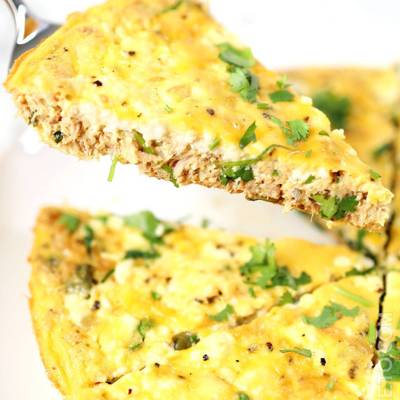 Golden slice of tuna frittata with creamy ricotta filling garnished with chopped cilantro.