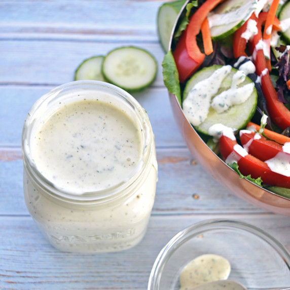 a jar of homemade ranch dressing next to a bowl of salad and a bowl with a ranch covered spoon