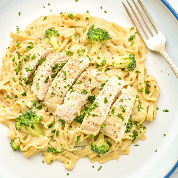 instant pot chicken fettuccini alfredo with broccoli on a blue rimmed plate with a fork