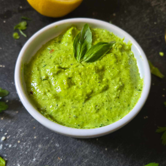 A bright, vibrant green pesto in a white bowl on a black cutting board.