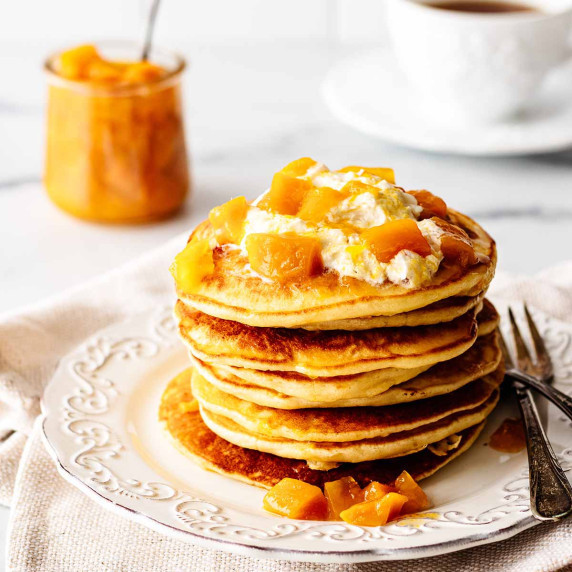 Stack of mango pancakes topped with mango compote on a white plate with two forks