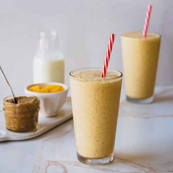 Two mango protein smoothies in tall glasses with red and white straws 
