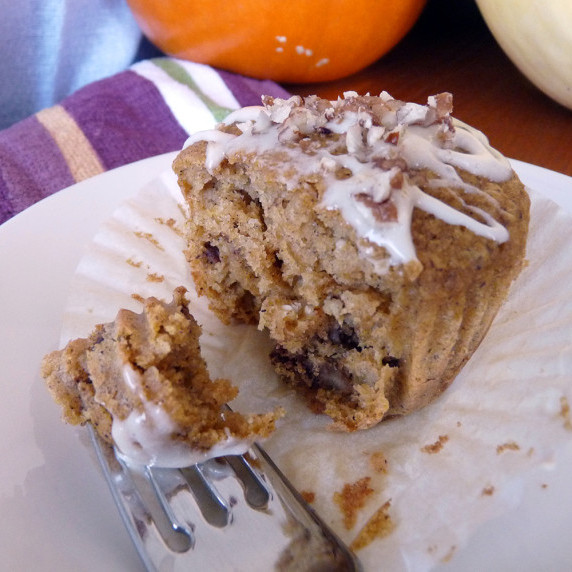 A maple pecan double pumpkin muffin on a plate with a bite on a fork, pumpkins in the background