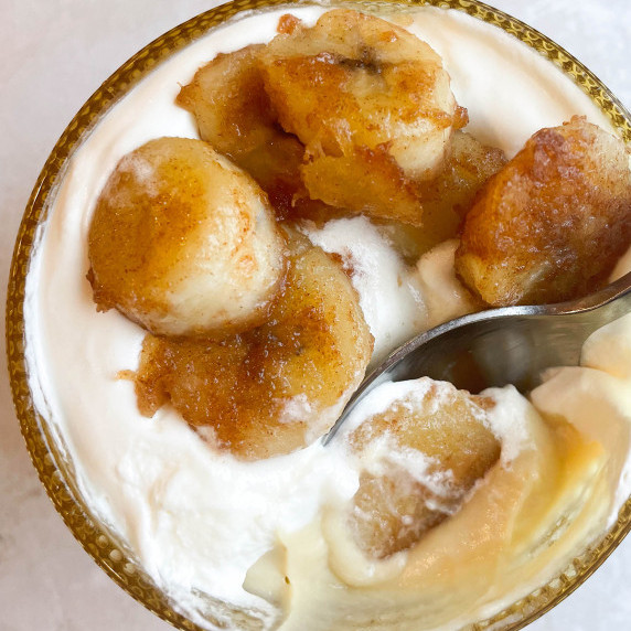 Pudding and whipped cream topped with caramelized bananas in an amber colored dessert glass.