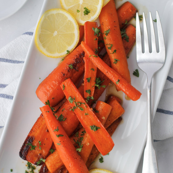 maple glazed carrots on a white serving dish with a fork with a kitchen towel
