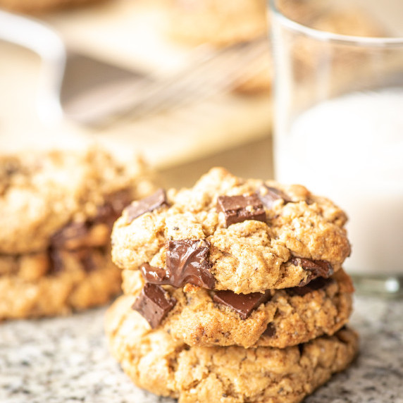 Chocolate chip cookies stacked on a countertop with a glass of milk