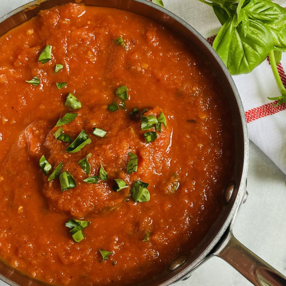 Marinara sauce in a saucepan garnished with fresh basil.