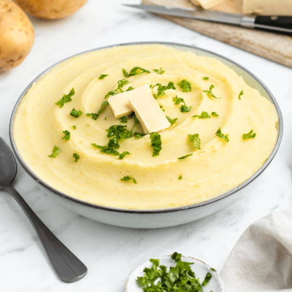 Mashed potatoes garnished with chopped parsley and butter slice in a white bowl with a spoon beside