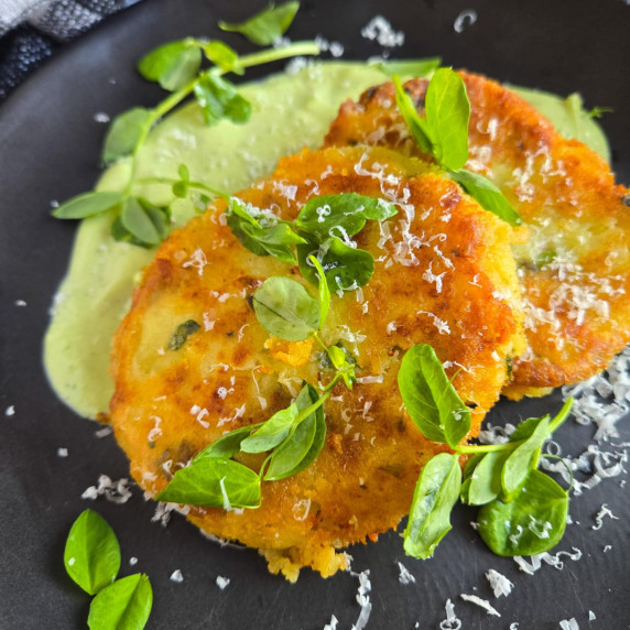 Golden brown patties topped with green shoots and a green sauce against a black plate.