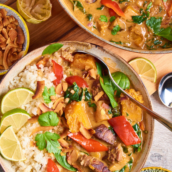 A bowl of Quick Massaman Lamb Curry with Veggies on cauliflower rice, topped with herbs, lime slices