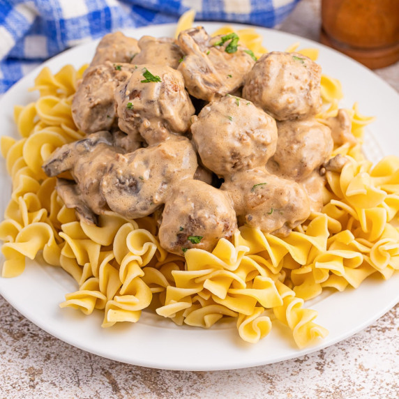 A square view of a plate of meatball stroganoff over noodles.