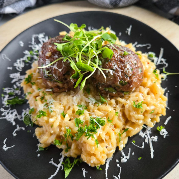 A bed of golden risotto topped with browned up meatballs and greens.