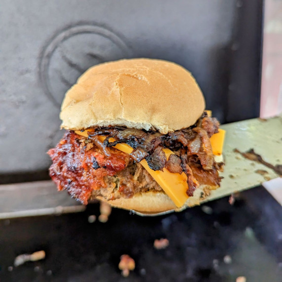 Meatloaf burger with mushroom relish on a spatula held over a Blackstone griddle. 