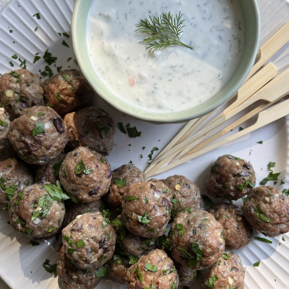 Cocktail meatballs served with feta dip, garnished with minced parsley on a white plate.
