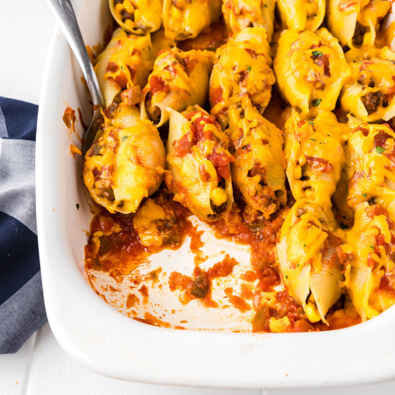 Taco stuffed shells being scooped with a spoon from a baking dish.