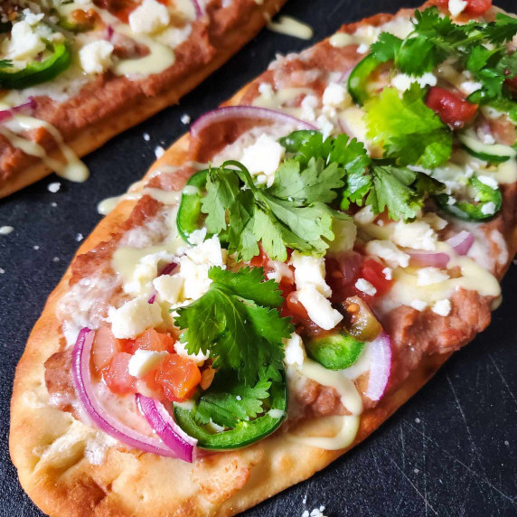 Flatbread topped with melty white cheese, green cilantro, and red salsa on a black cutting board.