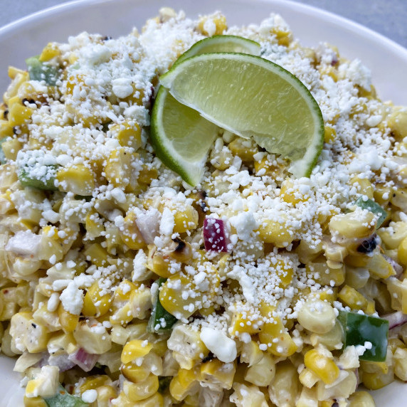 Corn salad with red onion, green pepper and feta cheese garnished with lime wedges.