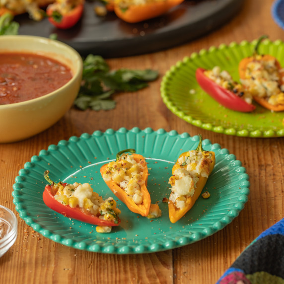 Three stuffed mini peppers on a teal colored plate with a bowl of salsa.