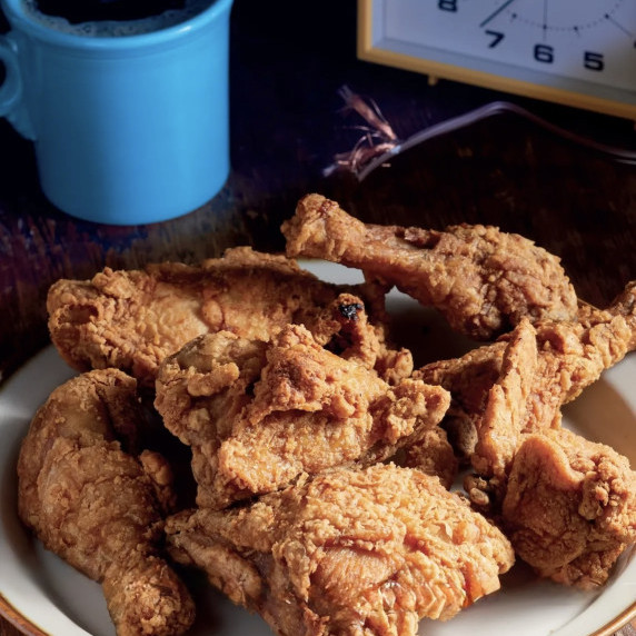 Crispy fried chicken on a rustic table with a blue mug and vintage clock.