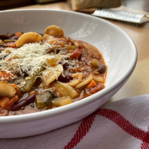 Minestrone soup topped with shredded parmesan cheese in a white bowl.