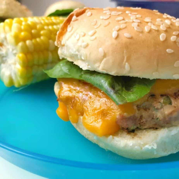 A close up of a turkey burger slider from the side with corn in the background.