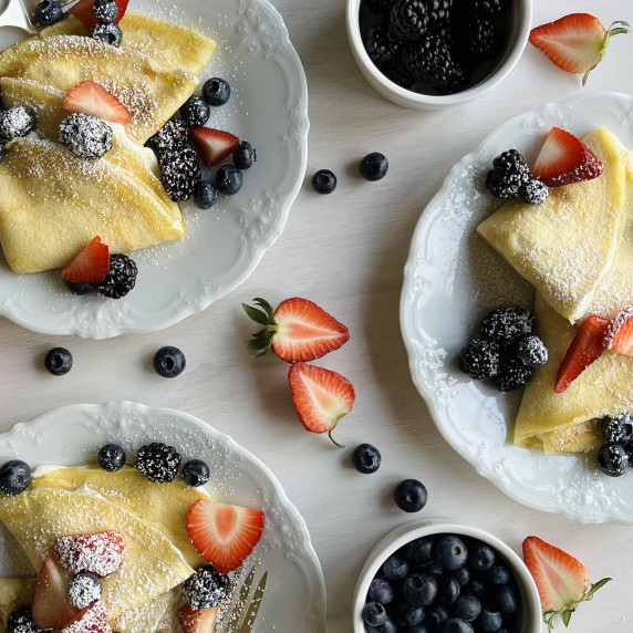 Three plates filled with cream cheese stuffed crêpes topped with fresh berries.