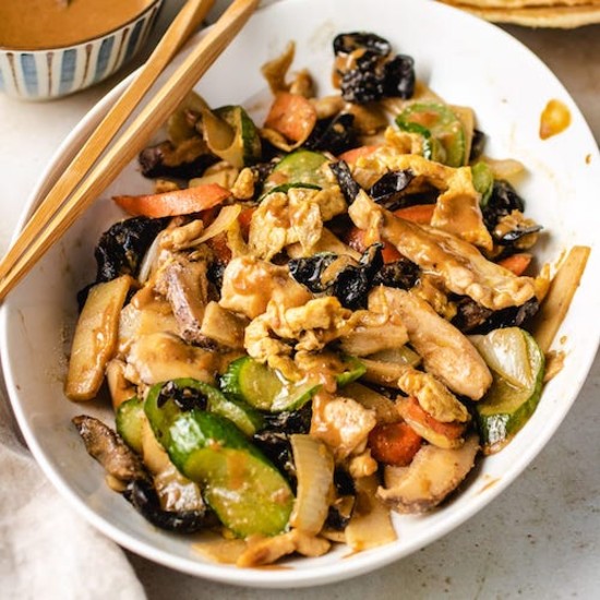 Chicken, cucumbers, onions, carrots and mushrooms with sauce in a white bowl with chopsticks