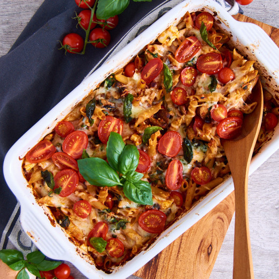 A casserole dish with Mushroom Spinach Pasta Bake with Black Garlic, topped with fresh cherry tomato