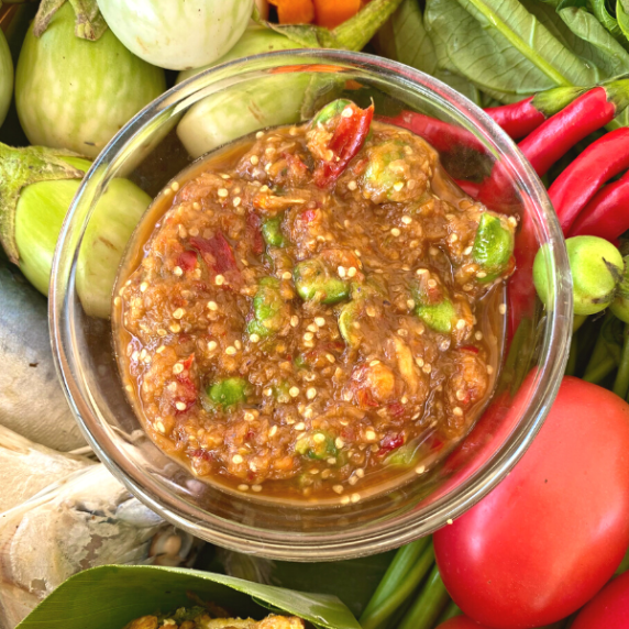 Nam prik kapi, a colorful Thai chili dip in a glass bowl, surrounded by red and green vegetables.