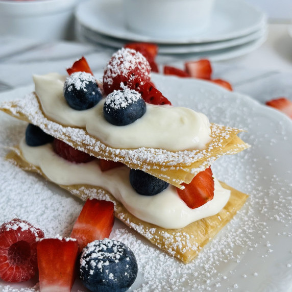 Phyllo dough layered with cream filling and fresh berries on a white plate.