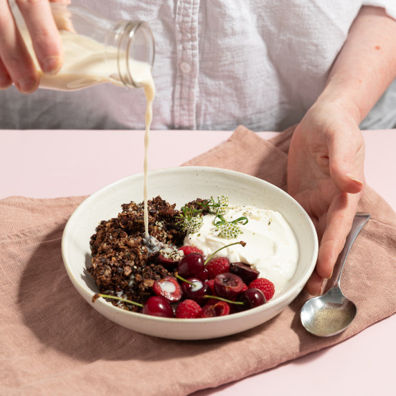 Hand pouring milk into a bowl of cherry chocolate granola