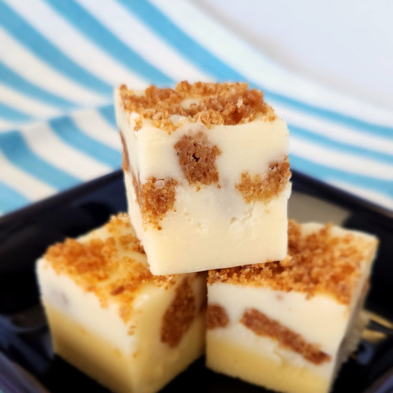 3 pieces of New York cheesecake fudge stacked on a dark blue dish with a striped background