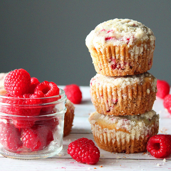 Raspberry muffins stacked on top of each other next to a small jar of fresh raspberries