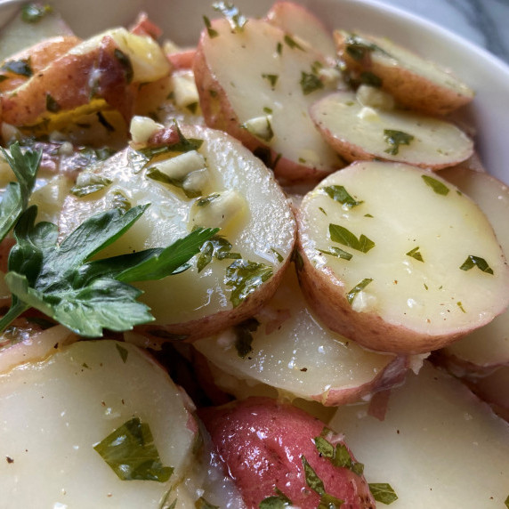 Sliced red potatoes and minced garlic tossed in vinegar and oil in a white bowl.