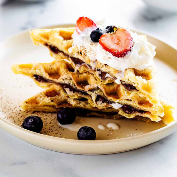 Stack of Nutella waffles topped with whipped cream and fresh berries on a white plate 