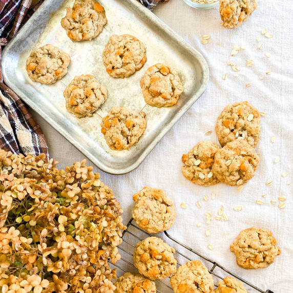 oatmeal scotchies cookies on a baking sheet and cooling rack on a white tablecloth
