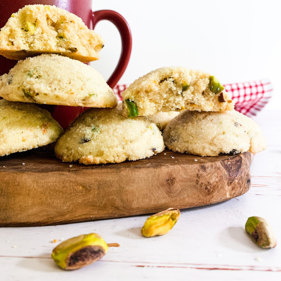 stacks of orange pistachio tea cakes on a wooden slab with pistachios and a cup of tea
