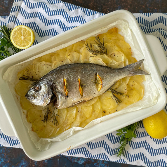Sea Bream over baked potatoes in a white pan.