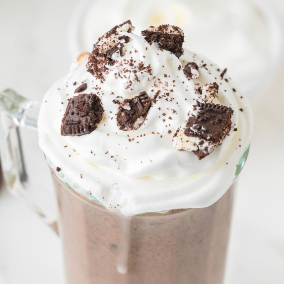  A glass mug filled with Oreo hot chocolate topped with whipped cream and crushed cookies.